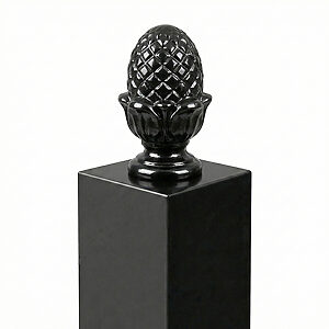 光沢のある黒い四角い柱の平らな頂部中央に載せられた、詳細な装飾が施された黒いパイナップル型のフィニアル（ポストキャップ）。鋳物のような質感がある。背景は白一色。